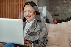 Close up of smiling asian business woman working laptop sitting in cozy office