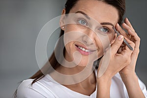 Close up smiling beautiful woman tweezing eyebrows with tweezers