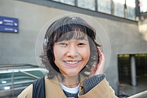 Close up of smiling brunette girl in headphones, listens music, travels around city, commutes to work, stands on a