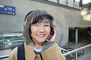 Close up of smiling brunette girl in headphones, listens music, travels around city, commutes to work, stands on a