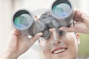 Close up of smiling businessman looking through binoculars, blue reflection in the glass