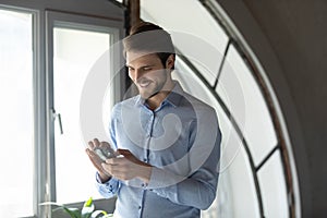 Close up smiling businessman using smartphone, standing in office