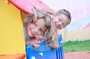 Close up of smiling childs face hiding behind wooden element of slide at playground on summer day.