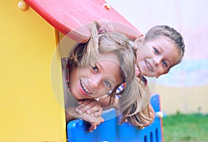 Close up of smiling childs face hiding behind wooden element of slide at playground on summer day.