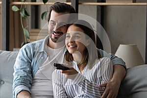 Close up smiling couple watching tv together, using remote controller