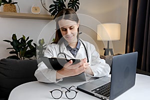 Close up of smiling doctor woman filling paper medical records. Practitioner in white coat doing paperwork at workplace with