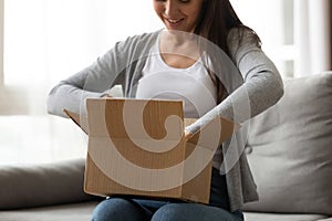 Happy young woman unboxing cardboard parcel at home. photo