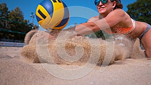 CLOSE UP: Smiling female volleyball player dives and strikes ball with her hands