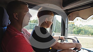 Close up of smiling ginger child holds the big steering wheel sitting on lap of father and learning to drive the truck