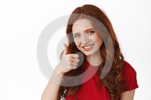 Close up of smiling ginger girl support your choice, praising good job, show thumb up in approval, say yes and recommend