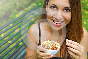 Close up smiling girl eating snack mix of nuts sitting in the park