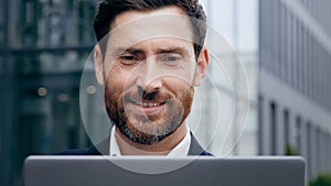 Close-up smiling handsome young man looking at laptop screen happy businessman surfing internet outdoors male journalist