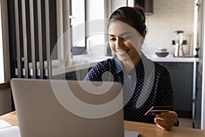 Close up smiling Indian woman paying online, using laptop