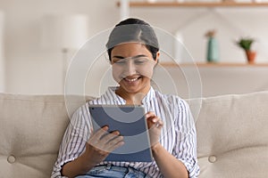 Close up smiling Indian woman using tablet, sitting on couch