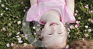 Close-up smiling little cute baby girl lying on green grass holding flowers looking at camera