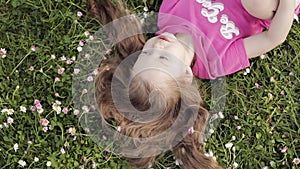 Close-up smiling little cute baby girl lying on green grass holding flowers looking at camera