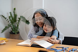 Close up smiling mature grandmother reading book to little granddaughter, telling interesting fairytale story, loving