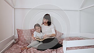 Close up of smiling mom and little daughter relax in cozy bed read funny interesting children book