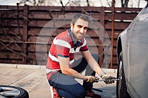 Close up smiling portrait of working man and changing tires using wrench, jack and hydraulic tools