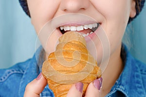 Close-up of a smiling pretty Caucasian woman in casual clothes holding a croissant. Front view from low angle. Indoors