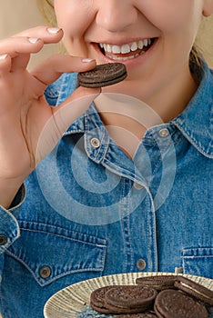 Close-up of a smiling pretty Caucasian woman holding a chocolate chip cookie in her hand. Front view from low angle. Vertical