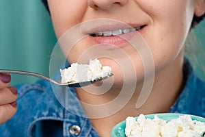 Close-up of a smiling pretty Caucasian woman holding a spoon and a bowl of cottage cheese in her hands. Front three-quarter view.