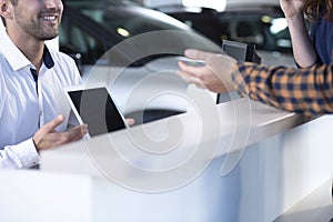 Close-up of smiling professional car seller with tablet offering