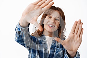 Close up of smiling redhead girl with freckles and white smile, look through hand frames gesture, taking shot of moment