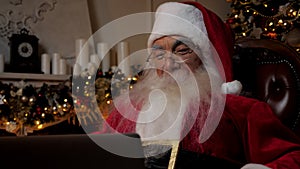 Close up smiling Santa Claus greets talks to children online laptop video call