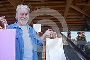 Close-up of a smiling senior man white haired doing shopping for christmas in a mall, looking at the camera while holding many