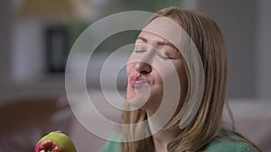 Close-up smiling woman eating healthful apple looking at camera smiling. Positive confident Caucasian slim attractive