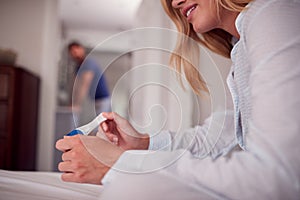 Close Up Of Smiling Woman Wearing Pyjamas In Bedroom Holding Positive Pregnancy Test