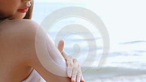 Close up Smiling young asian woman applying a sunscreen lotion on shoulder her skin on a seaside beach tropical resting and relaxa