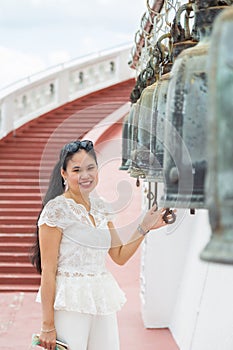 Close up smiling young Asian woman in a white shirt standing and touching a bell in Buddish temple