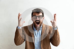 Close up Smiling Young Businessman making faces Wearing Eyeglasses, Looking at the Camera Against Gray Wall