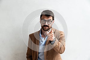 Close up Smiling Young Businessman making faces Wearing Eyeglasses, Looking at the Camera Against Gray Wall