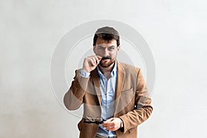 Close up Smiling Young Businessman making faces Wearing Eyeglasses, Looking at the Camera Against Gray Wall