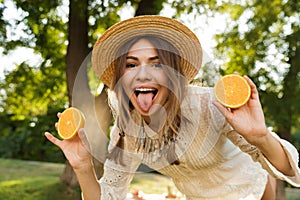 Close up of smiling young girl in summer hat spending time at the park, showing sliced orange,