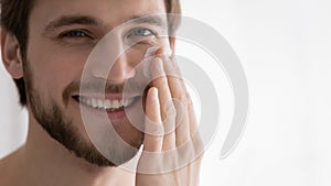 Close up smiling young man applying moisturizing face cream