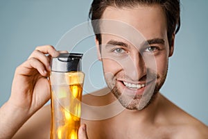 Close up of a smiling young nude man presenting shampoo