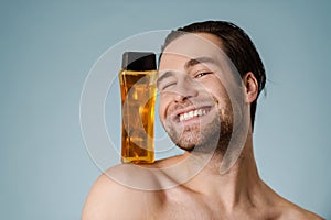 Close up of a smiling young nude man presenting shampoo