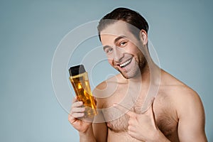 Close up of a smiling young nude man presenting shampoo