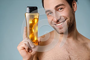 Close up of a smiling young nude man presenting shampoo