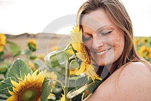 Close up of smiling young woman with eyes closed touching sunflower on face at field