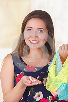 Close up of a smiling young woman, holding an assorted colorful underwears and a soft gelatin vaginal tablet or