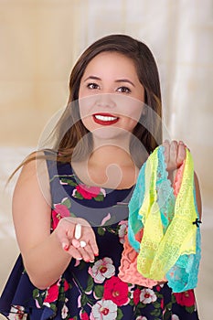 Close up of a smiling young woman, holding an assorted colorful underwears and a soft gelatin vaginal tablet or