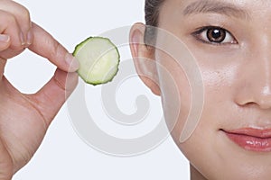 Close up of smiling young woman holding up a cucumber slice, studio shot