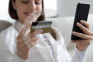 Close up smiling young woman using phone, holding credit card