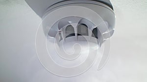 Close-up of smoke alarm on the ceiling surrounded by white smoke. Stock footage. Fire alarm at the house