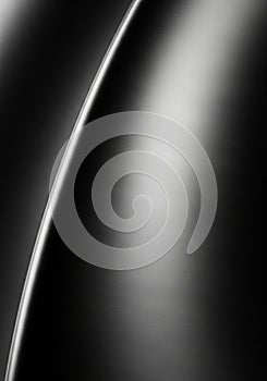 A close-up of a smooth, curved metallic surface with a brushed texture. The lighting